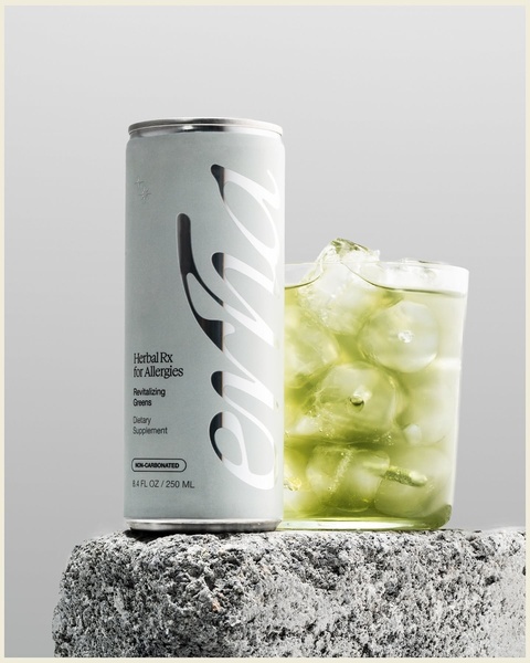 A high-end, studio-lit photograph of a single canned herbal supplement placed on a textured stone block beside a glass of green herbal tonic.